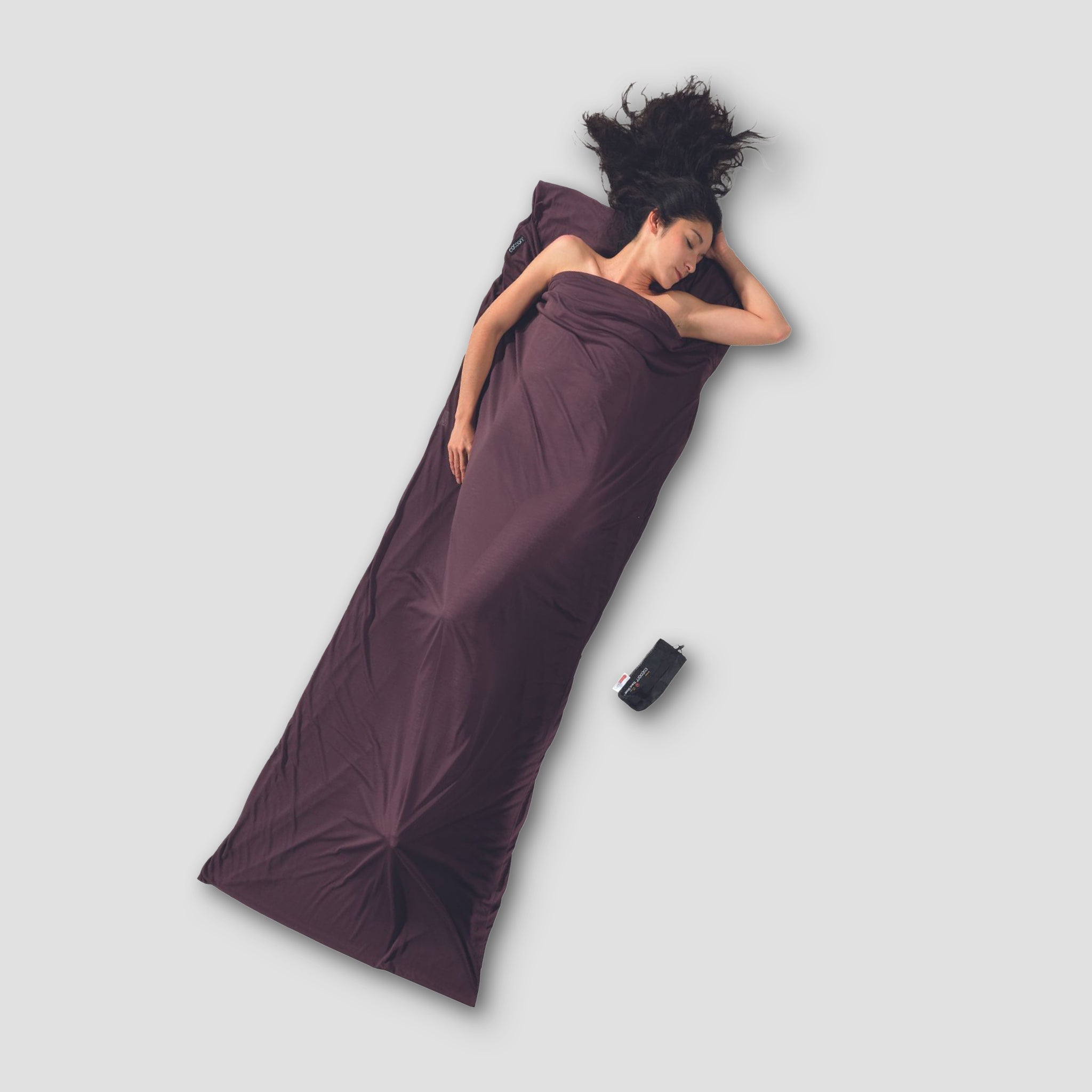 Woman lying on a purple sleeping bag on a light gray background
