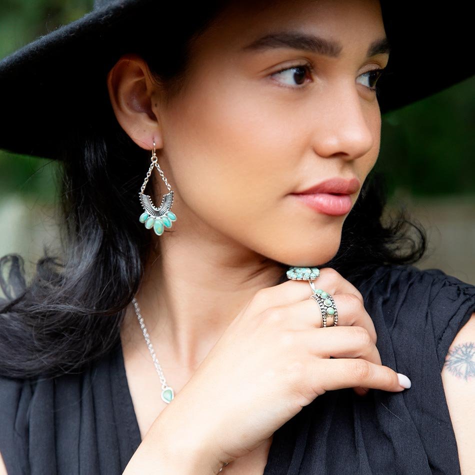 Woman wearing turquoise earrings and a ring, with a blurred natural background