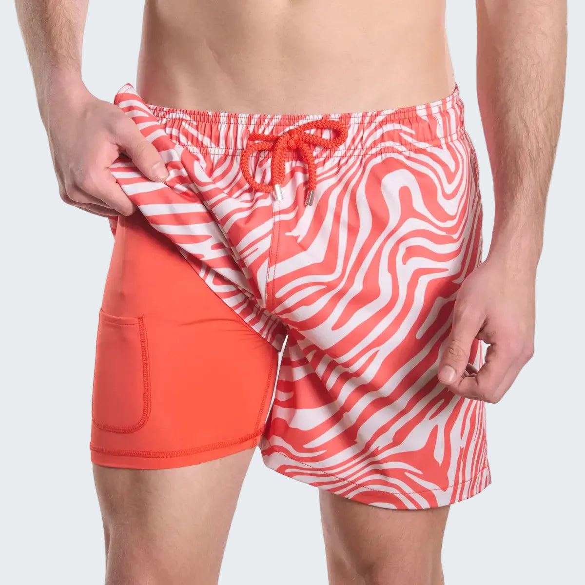 Two pairs of swim shorts, one with a red and white pattern and the other solid orange, on a white background.