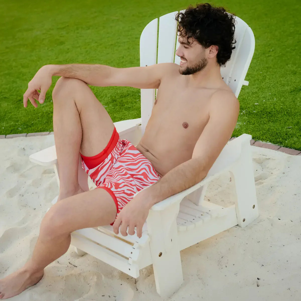Man sitting on a white chair in a sandy area with grass in the background