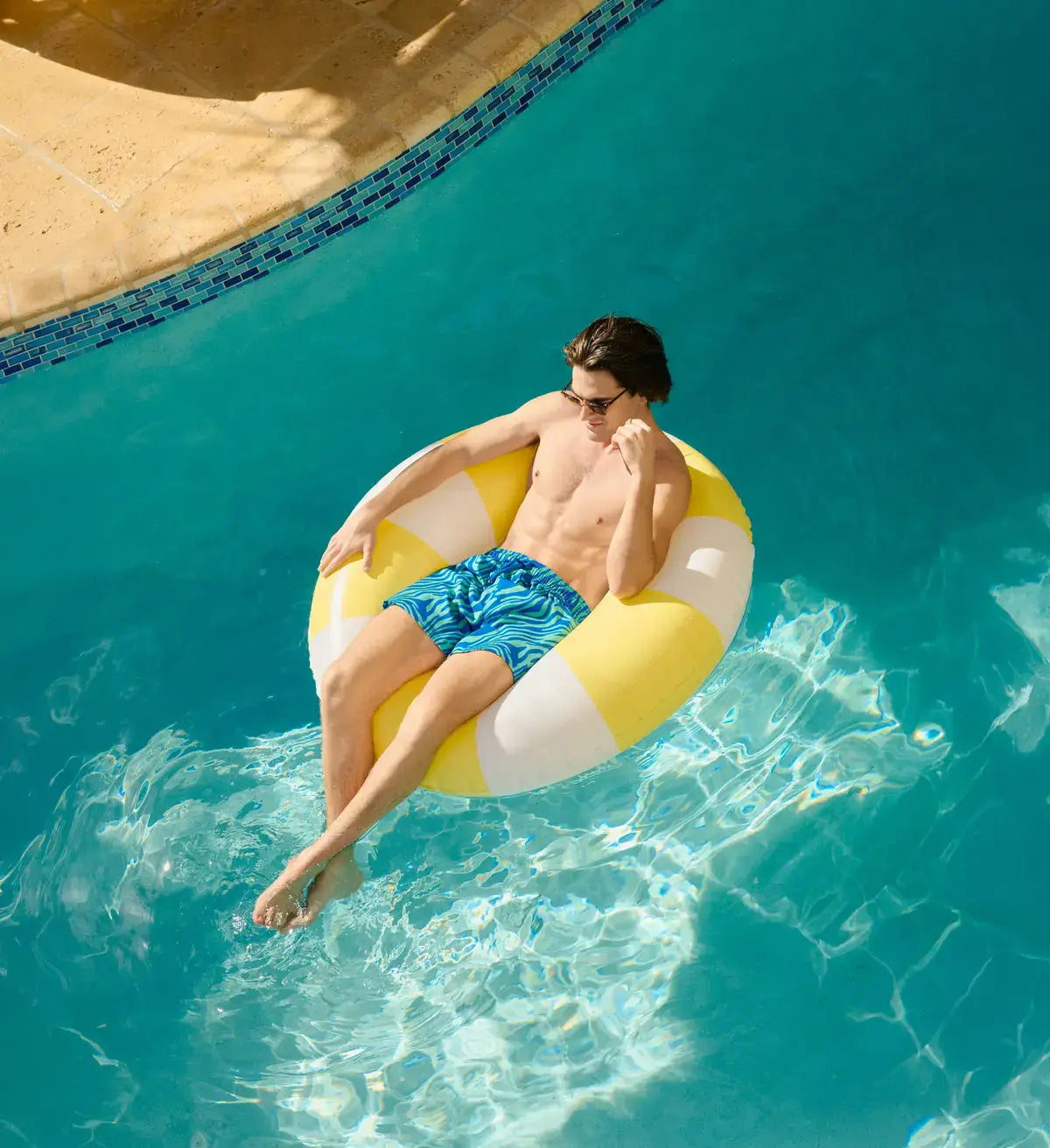 Man relaxing on a yellow and white inflatable ring in a pool