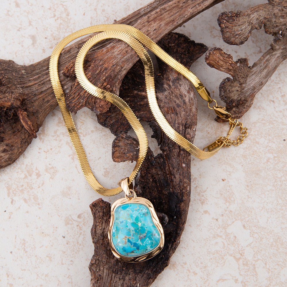 Gold necklace with a turquoise pendant on a natural wood background