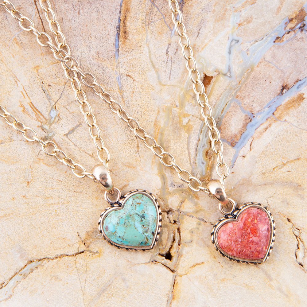 Two heart-shaped pendants on gold chains against a marble background