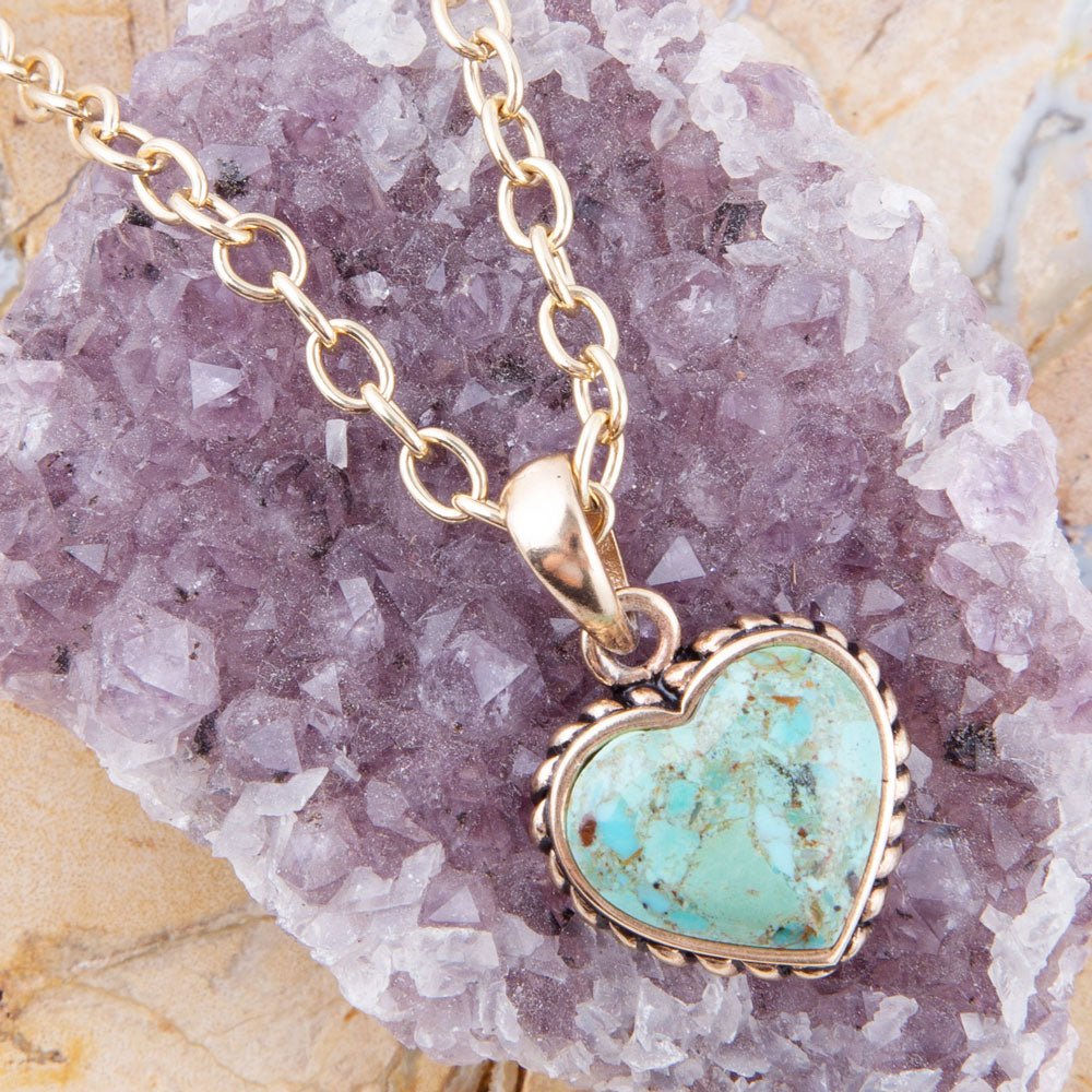 Turquoise heart-shaped pendant on a gold chain against a purple crystal background