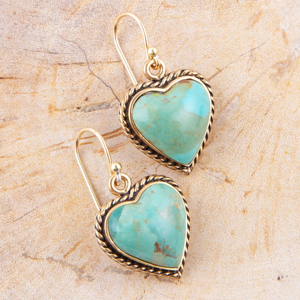 Turquoise heart-shaped earrings with gold frames on a beige stone background