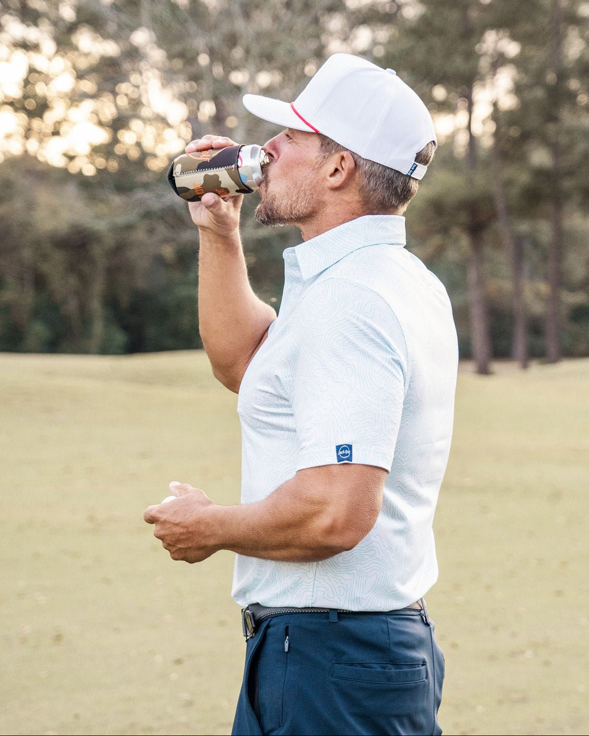 Man in golf attire drinking from a bottle on a golf course