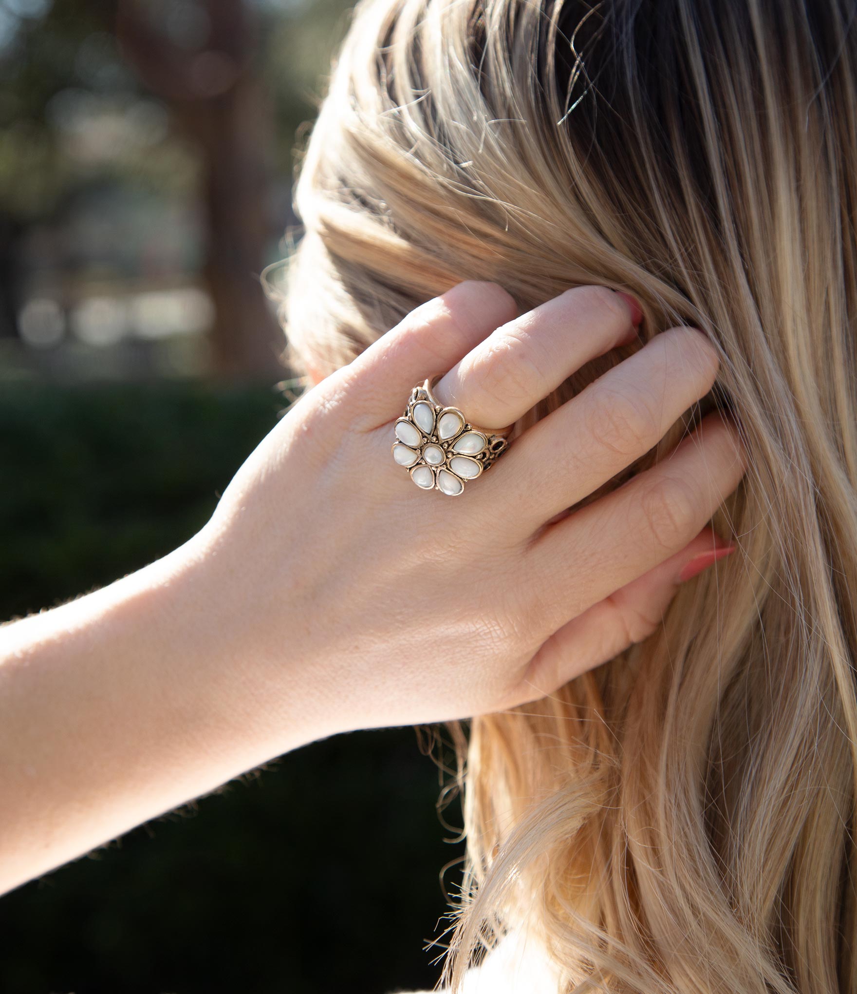 Close-up of a hand wearing a decorative ring with blurred outdoor background