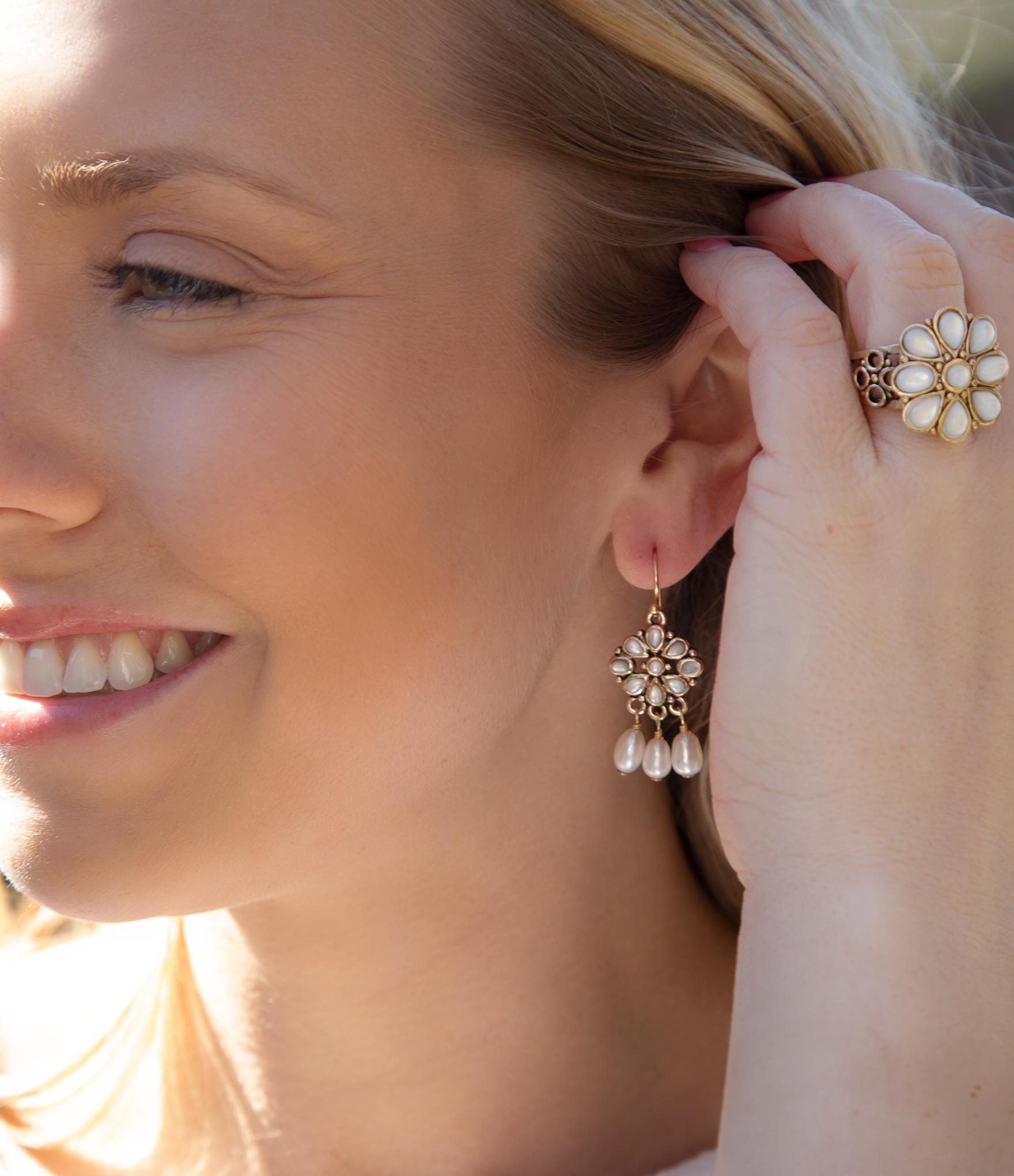 Woman wearing a floral earring with pearl drops, close-up of ear and hand.