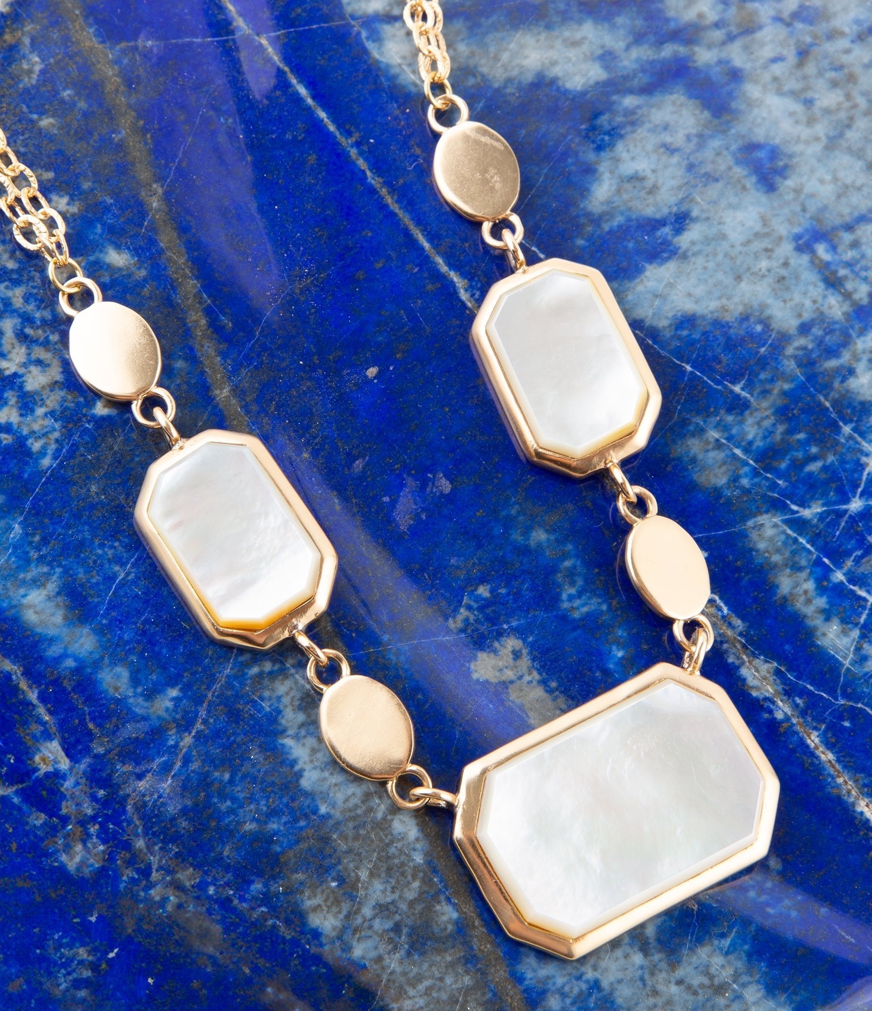 Necklace with gold and white stone pendants on a blue stone background