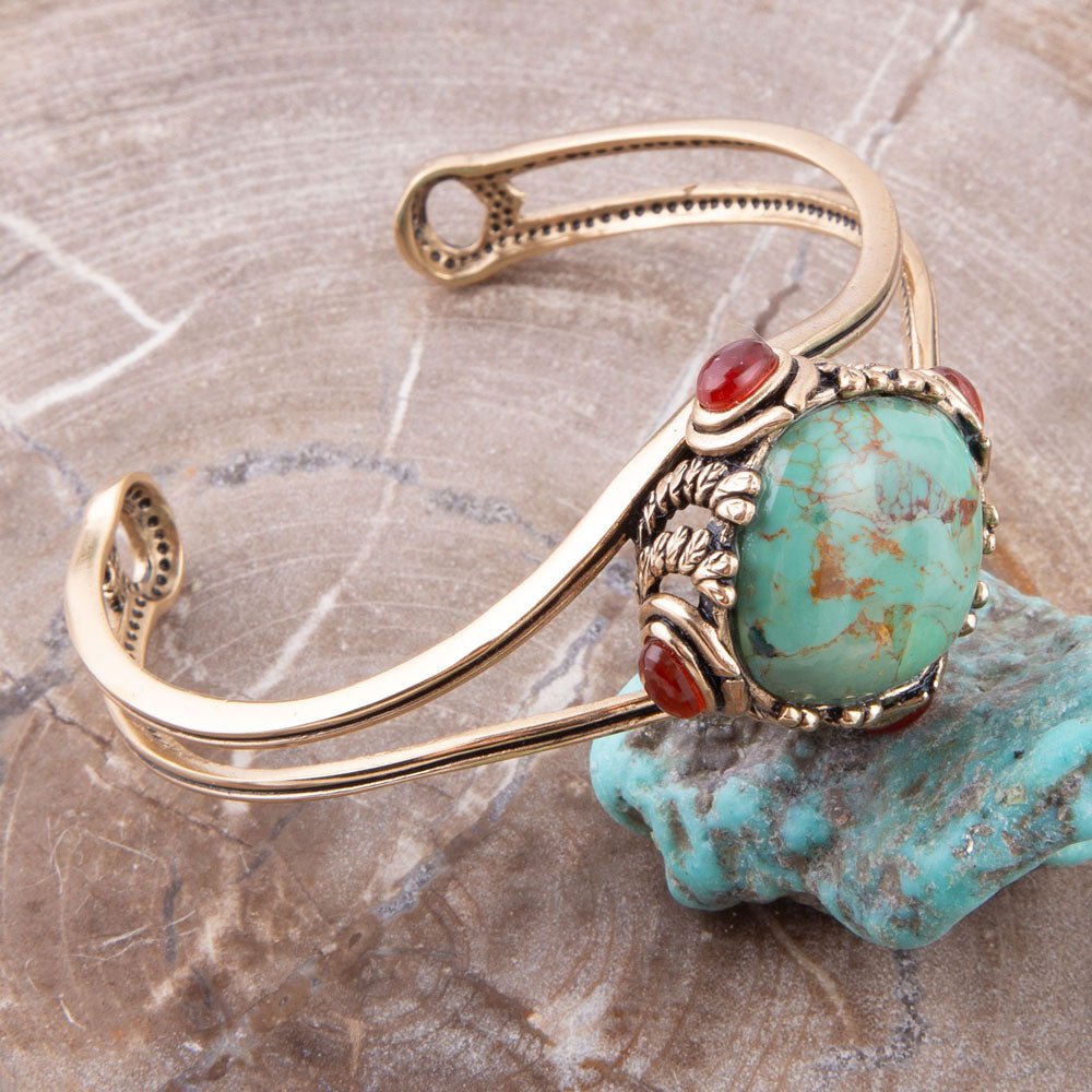 Gold bracelet with turquoise and red stone on a textured surface