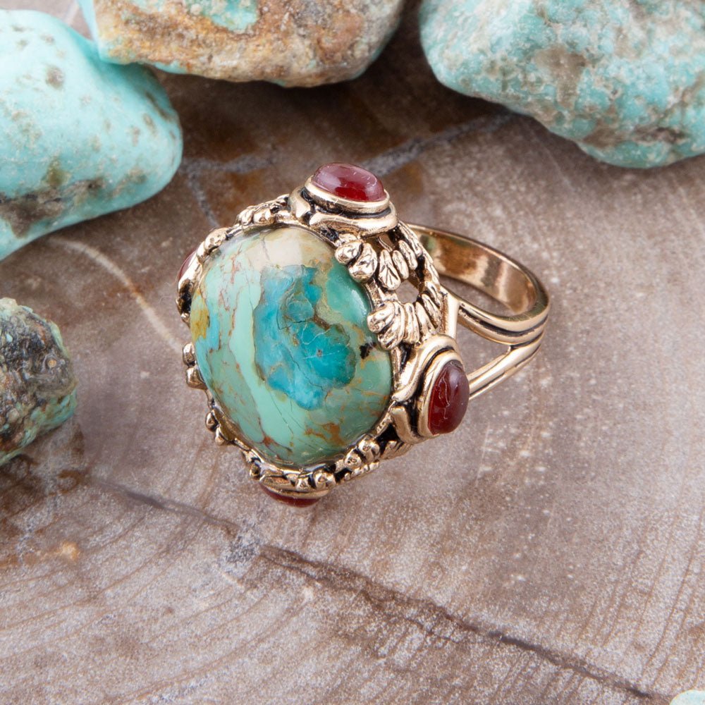 Gold ring with turquoise and red stone on a stone surface