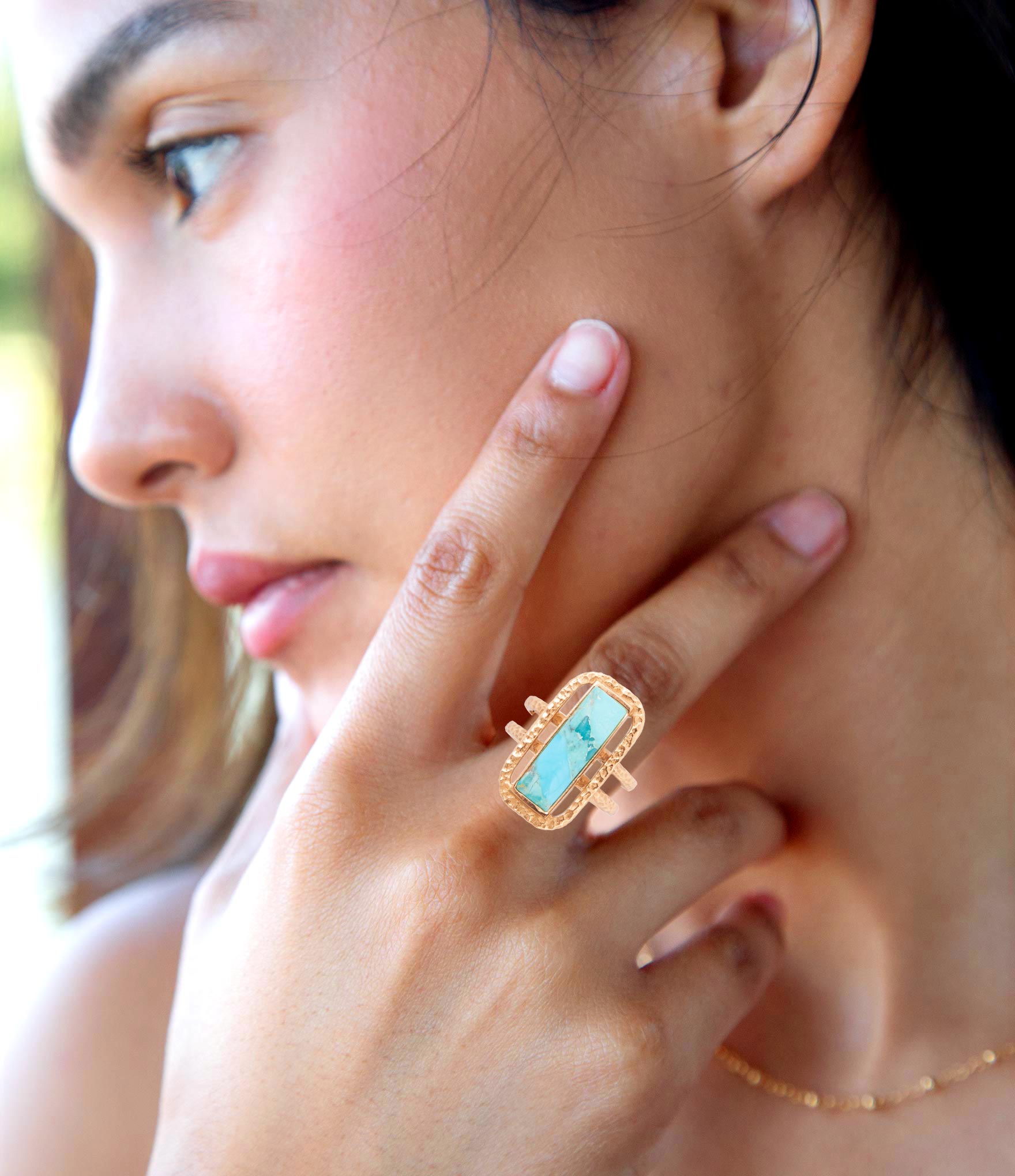 Close-up of a woman wearing a gold ring with a turquoise stone, outdoors.