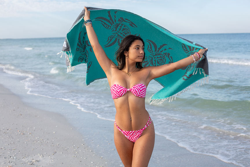 Woman in pink bikini holding a green towel on a beach