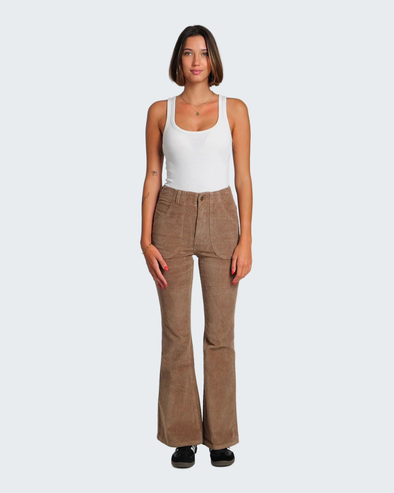 Woman wearing a white tank top and brown flared pants on a white background