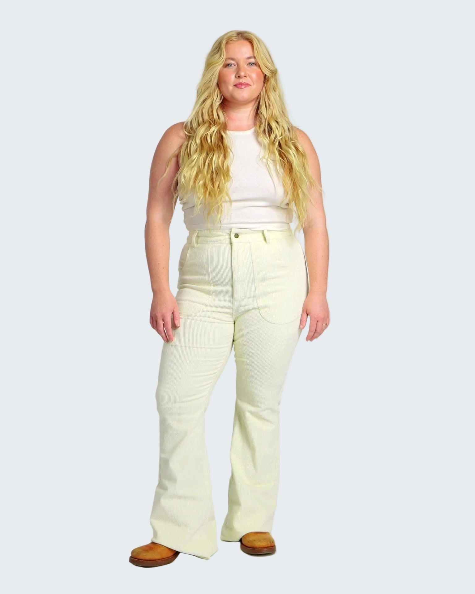 Woman wearing a white sleeveless top and light yellow pants on a white background
