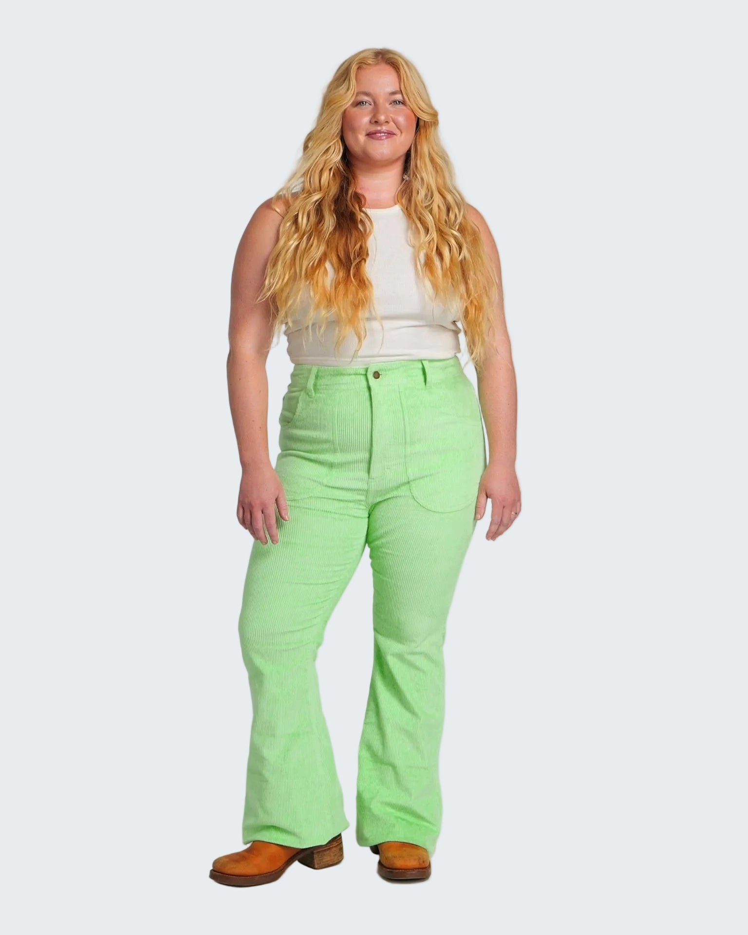 Woman wearing bright green pants and a white top on a plain background