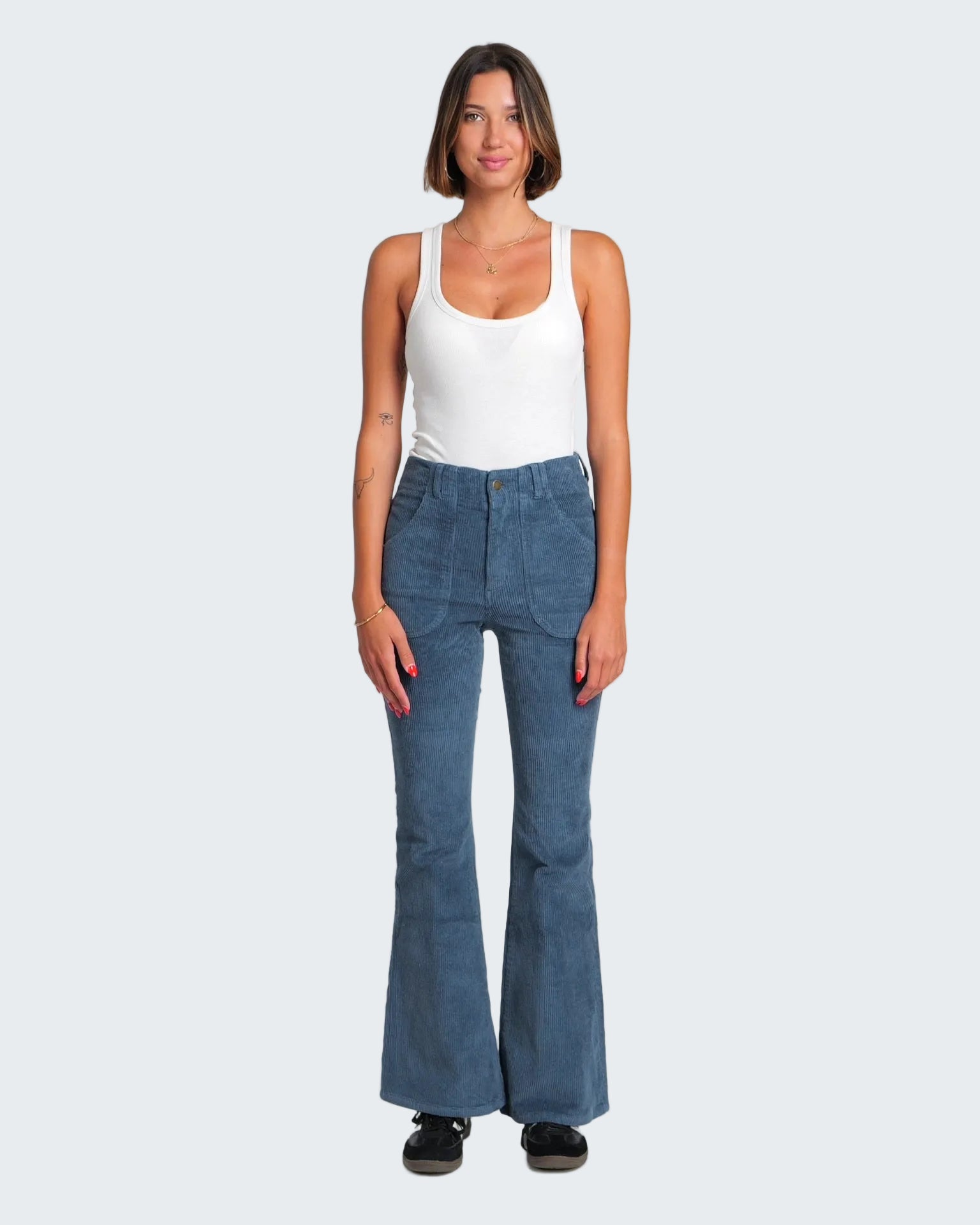 Woman wearing blue flared jeans and a white tank top on a white background