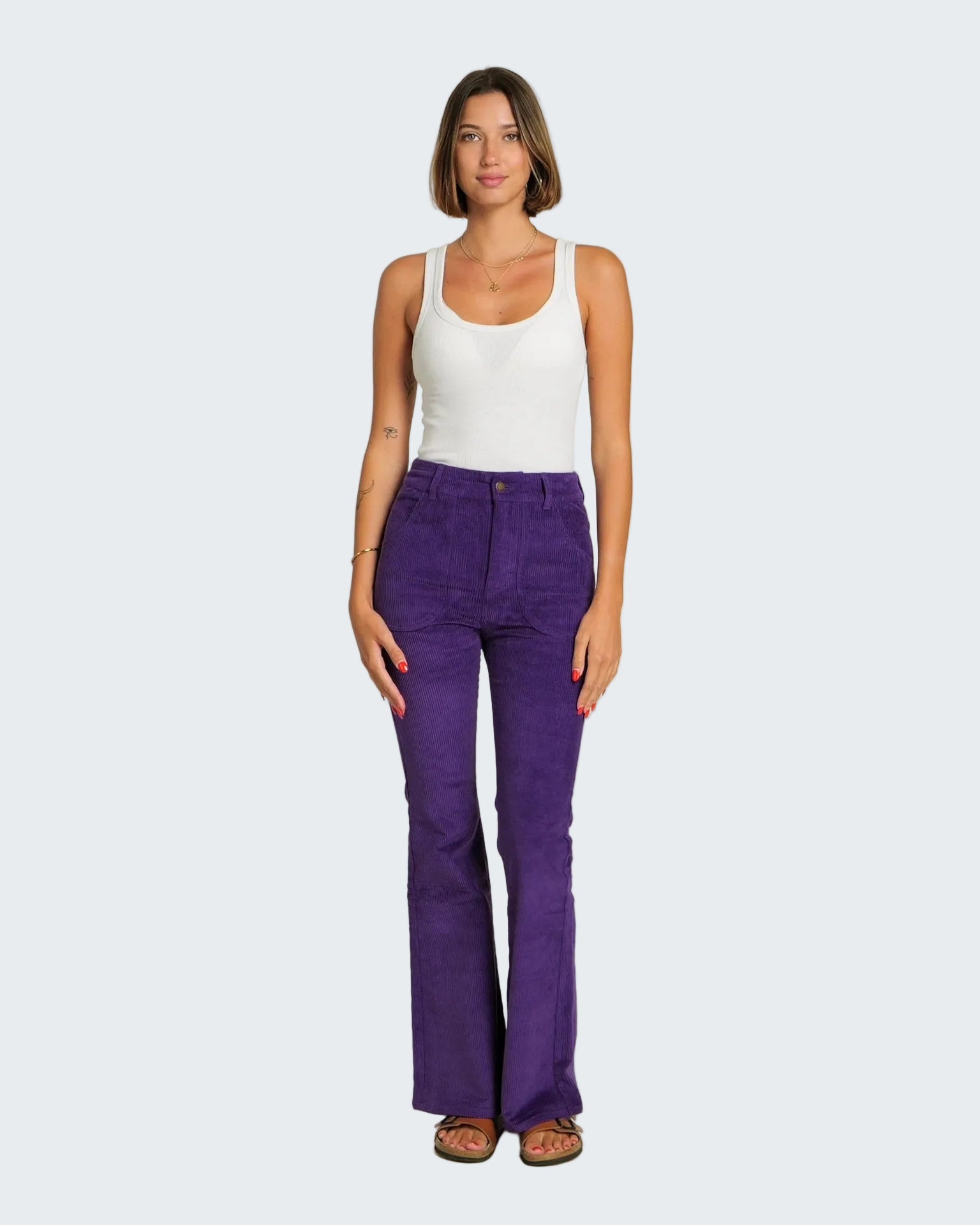Woman wearing purple pants and a white tank top on a white background