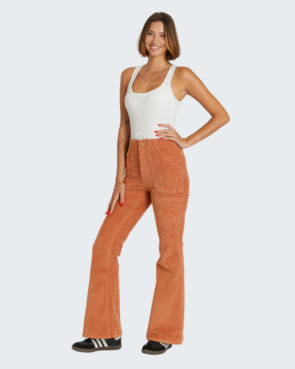 Woman wearing a white tank top and brown corduroy pants on a white background