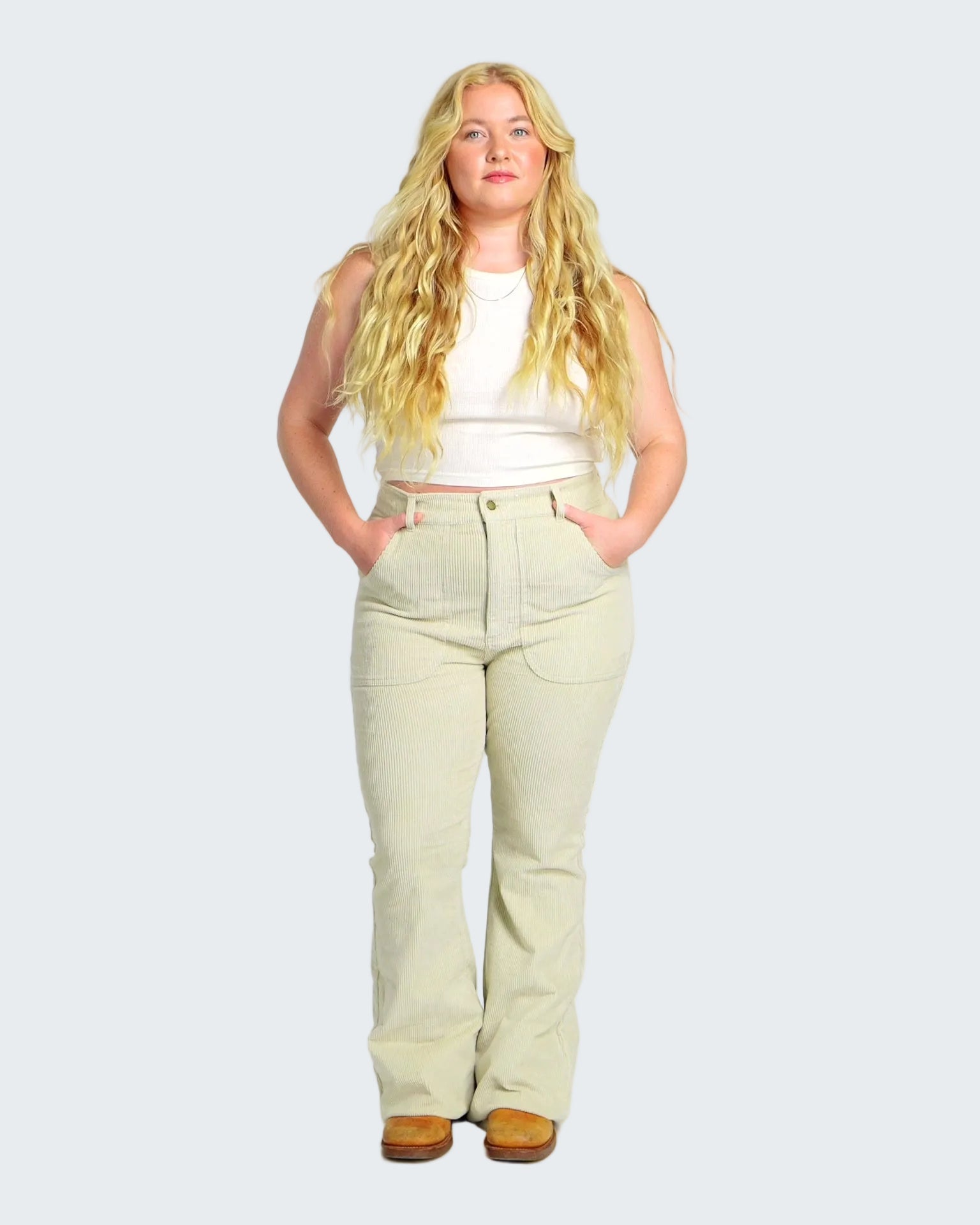 Woman wearing a white sleeveless top and light green pants on a white background