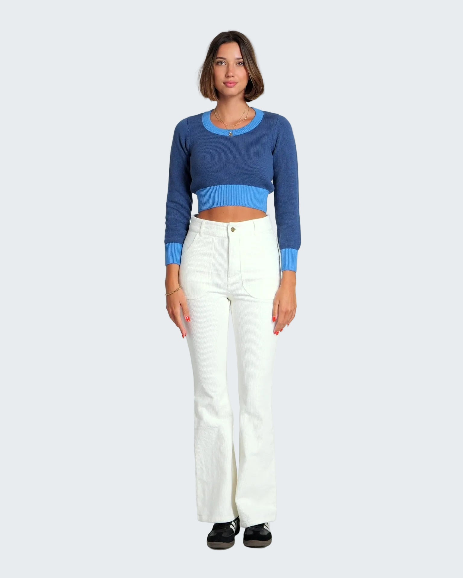 Woman wearing a blue cropped sweater and white pants on a white background