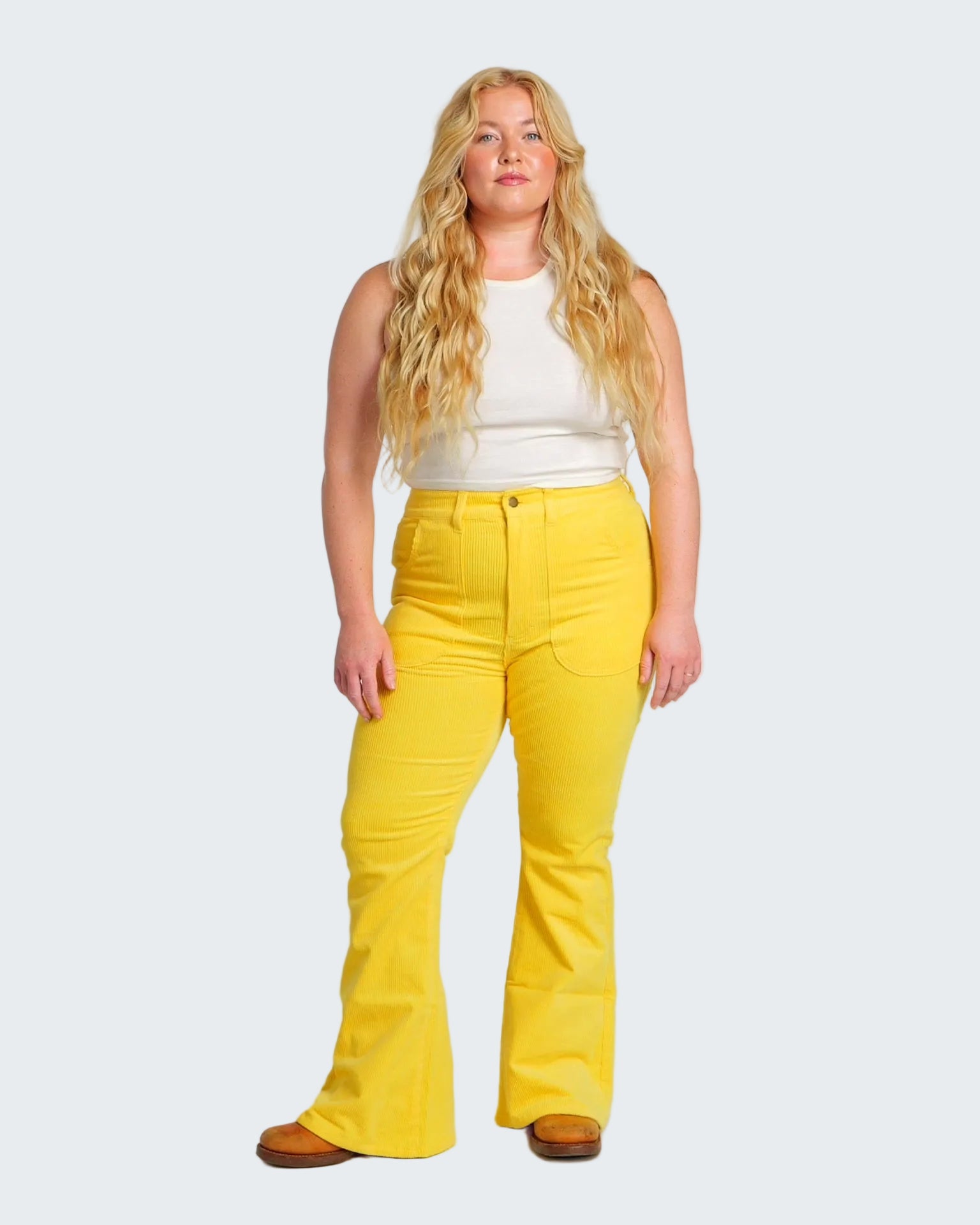 Woman wearing yellow pants and a white top on a plain background