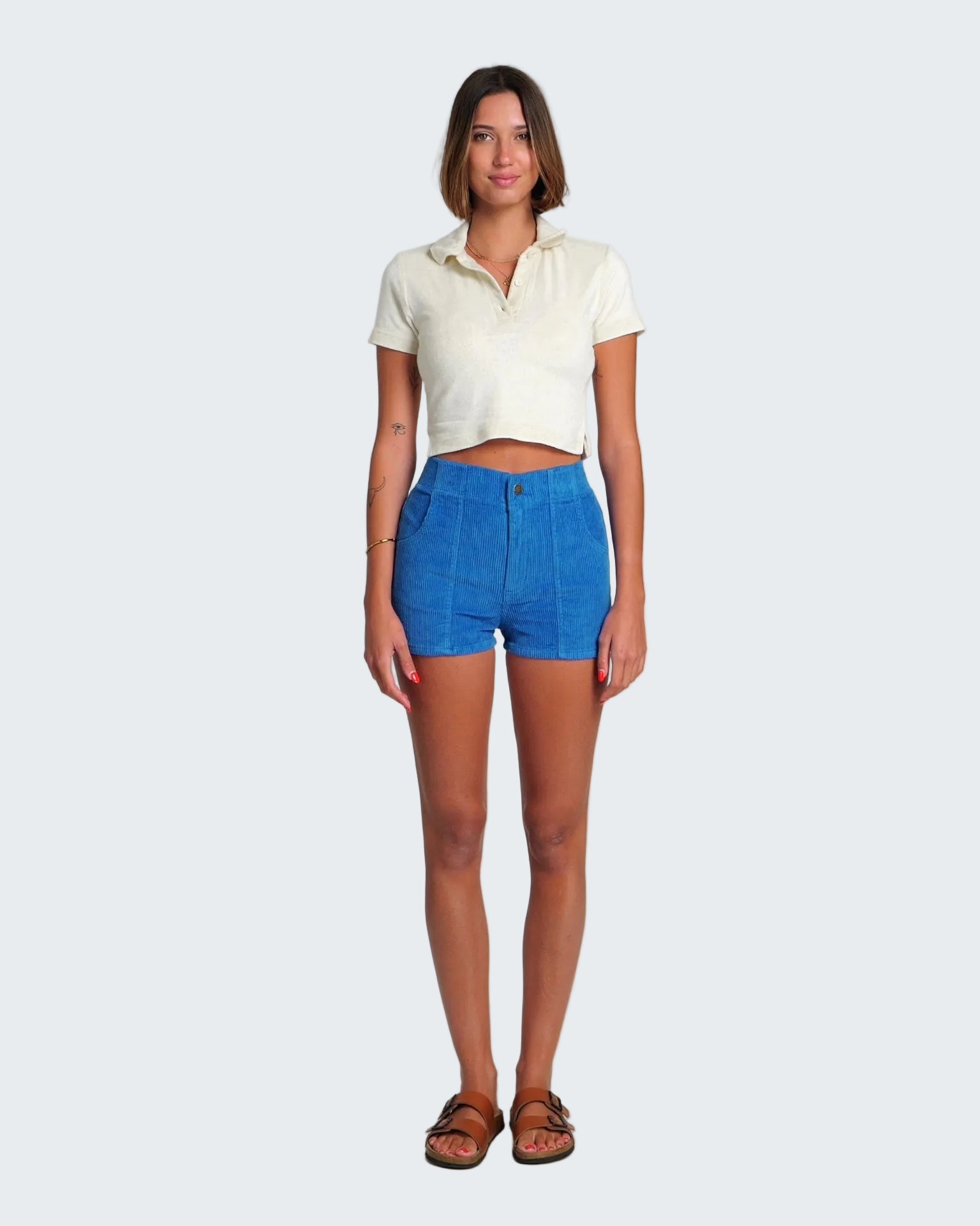 Woman wearing a white crop top and blue shorts on a plain background