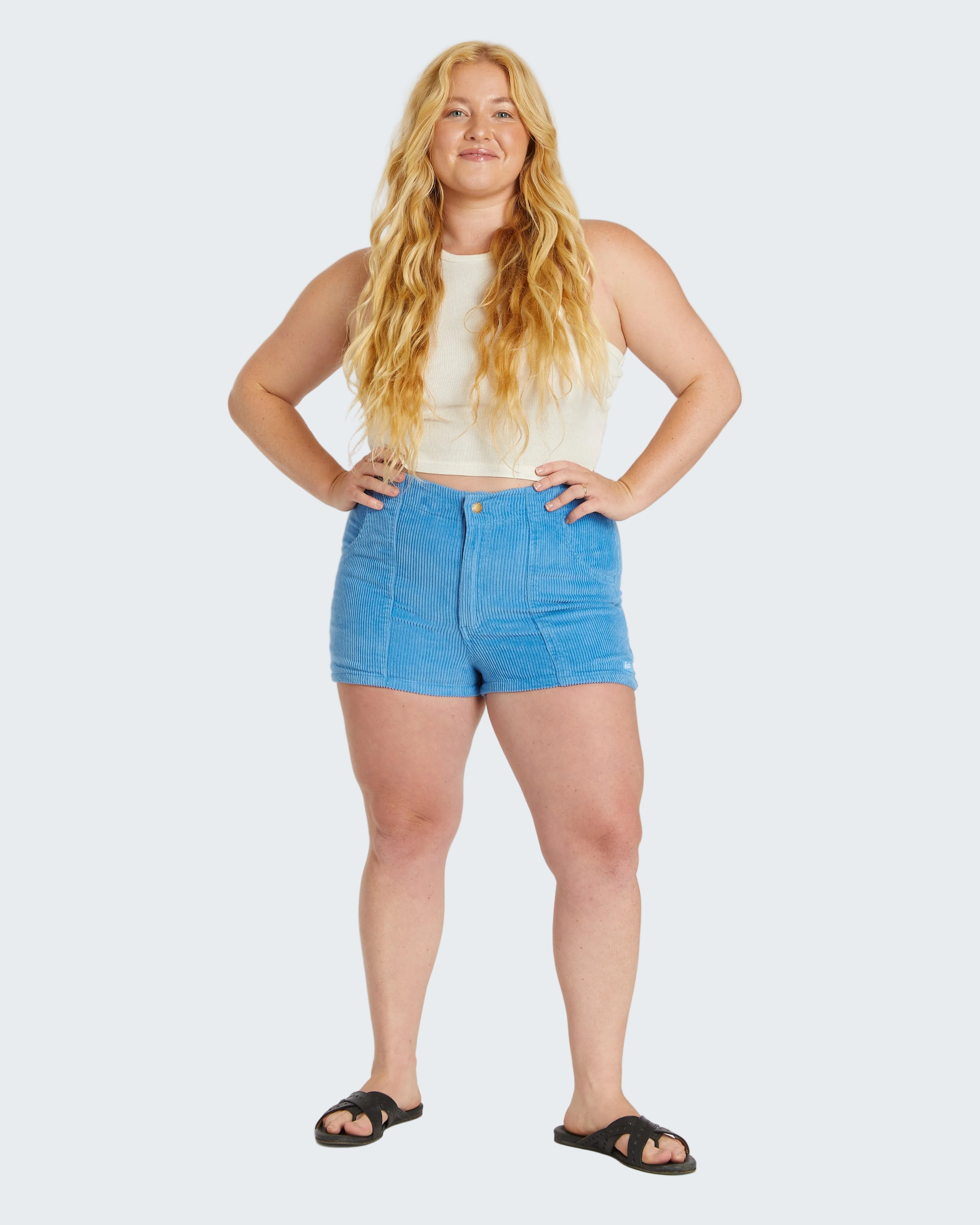 Woman wearing a white sleeveless top and blue denim shorts on a white background