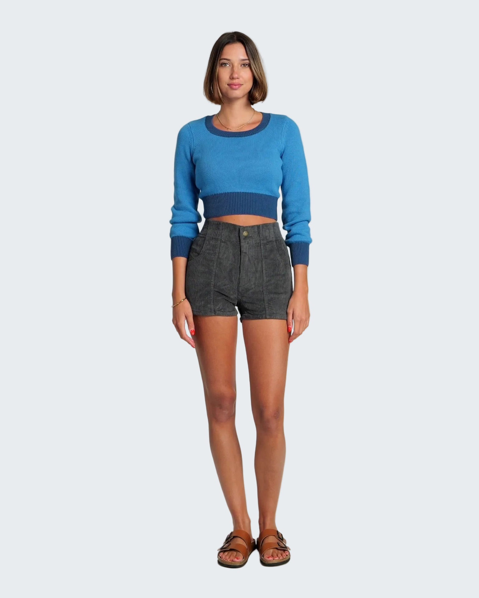 Woman wearing a blue sweater and dark shorts on a white background