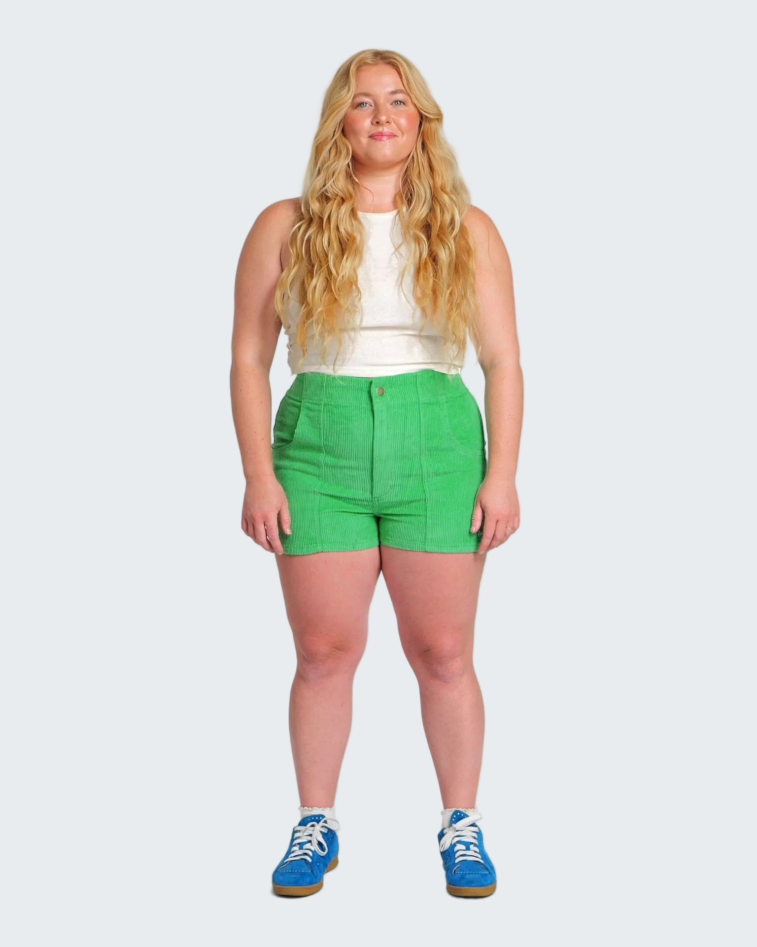 Woman wearing a white sleeveless top and green shorts on a white background