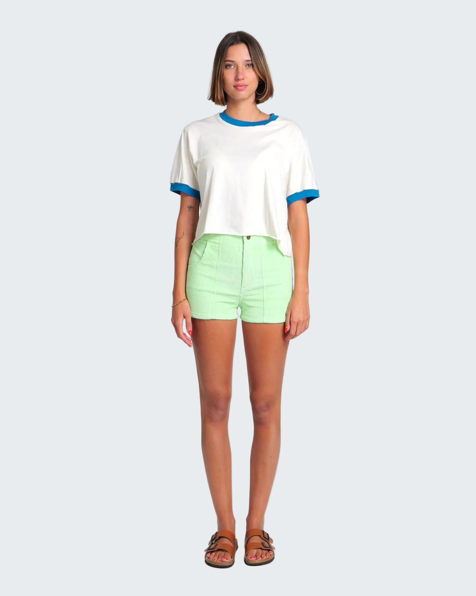 Woman wearing a white shirt with blue trim and light green shorts on a white background