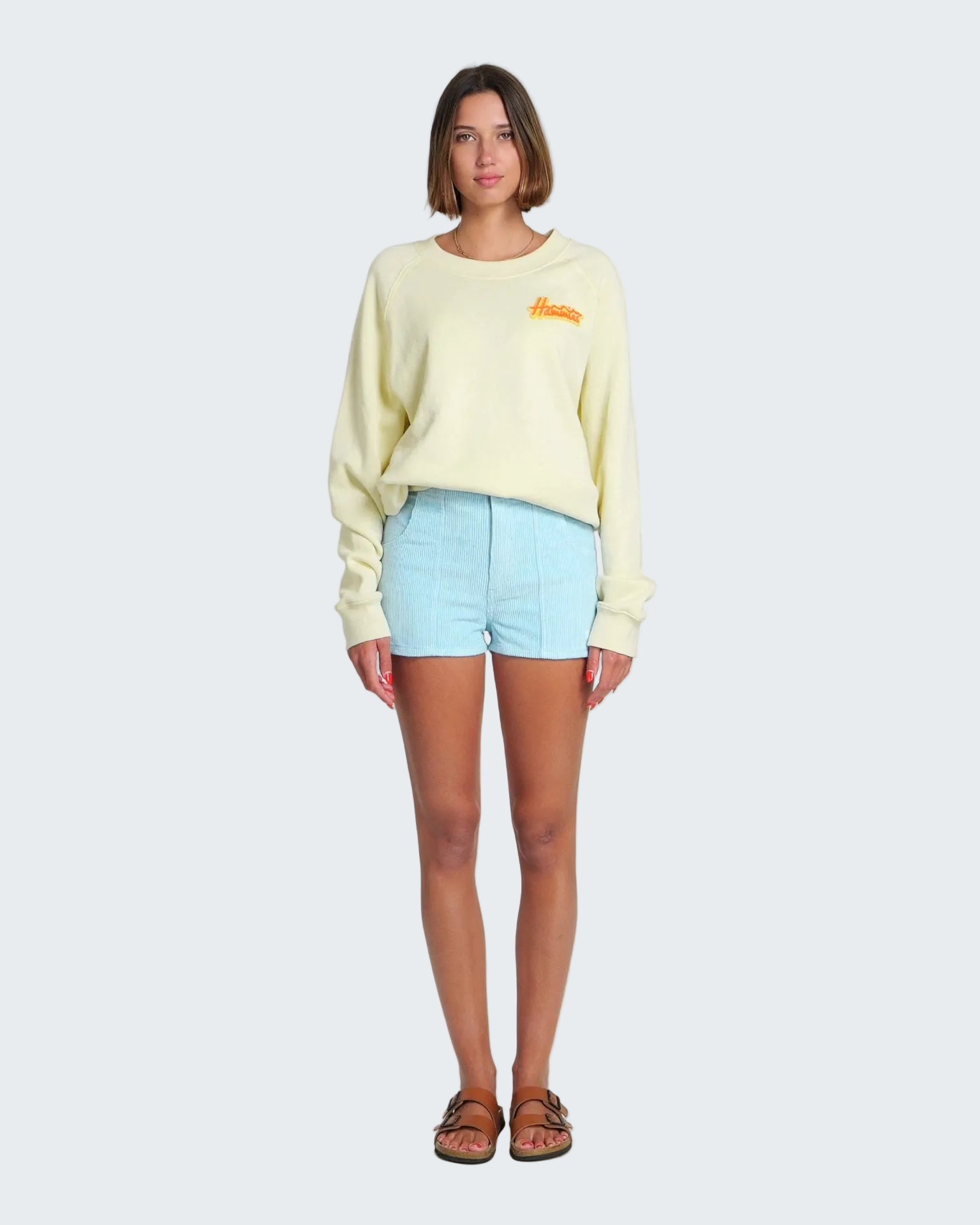 Woman wearing a light yellow sweater and light blue shorts on a white background