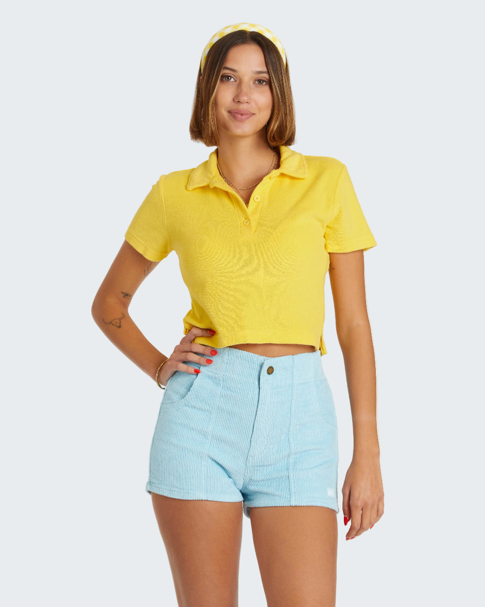 Woman wearing a yellow polo shirt and light blue shorts on a white background