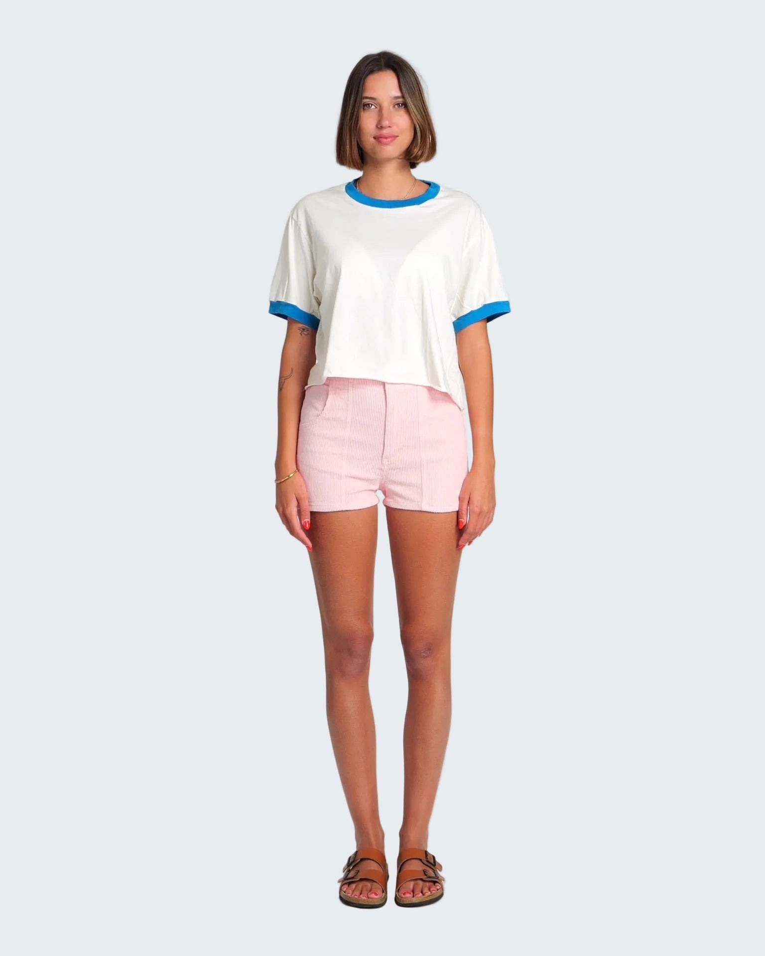 Woman wearing a white t-shirt with blue trim and pink shorts on a white background