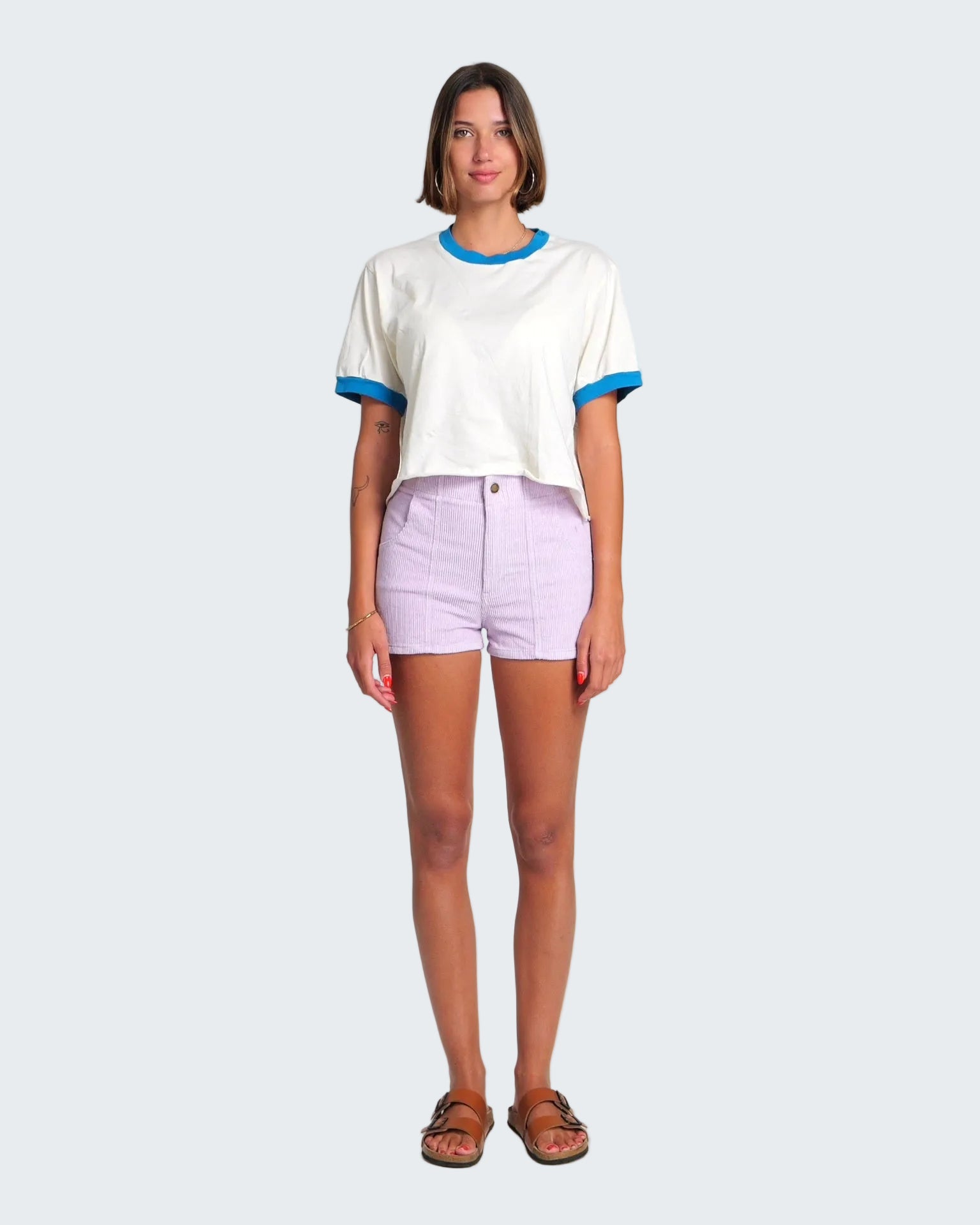Woman wearing a white t-shirt with blue trim and light purple shorts on a white background