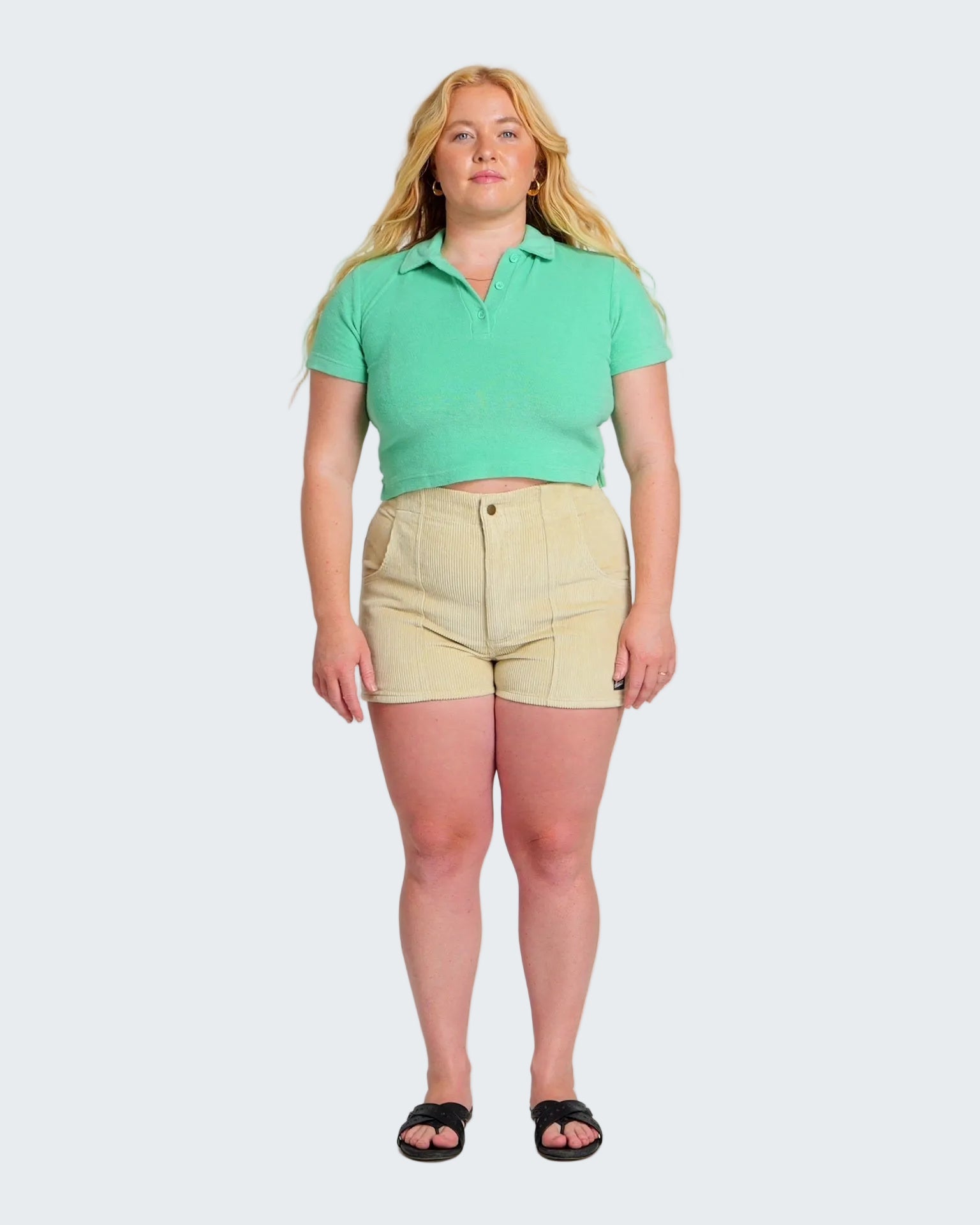 Woman wearing a green polo shirt and beige shorts on a white background