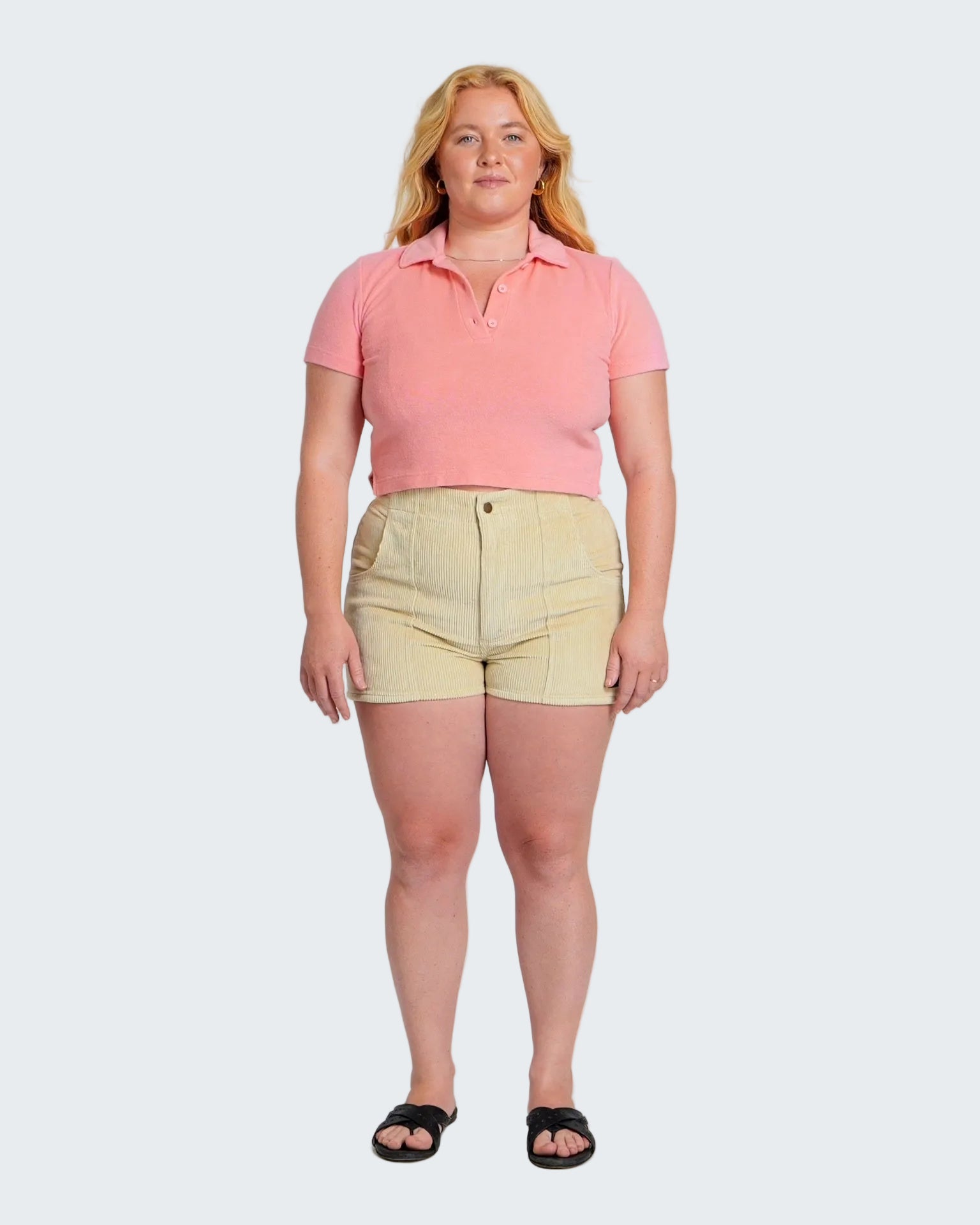 Woman wearing a pink polo shirt and beige shorts on a white background