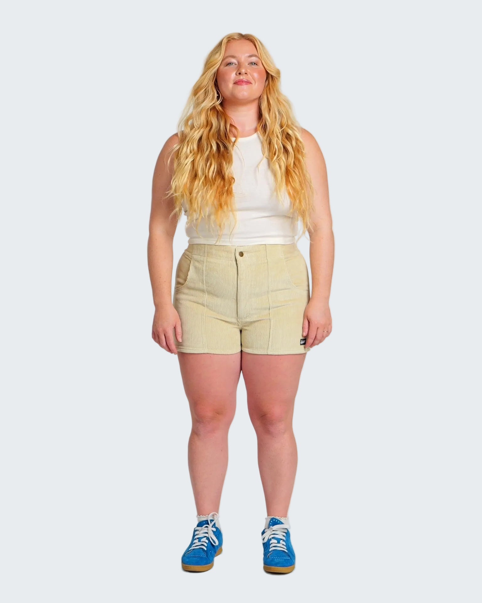 Woman wearing a white sleeveless top and light yellow shorts on a plain background