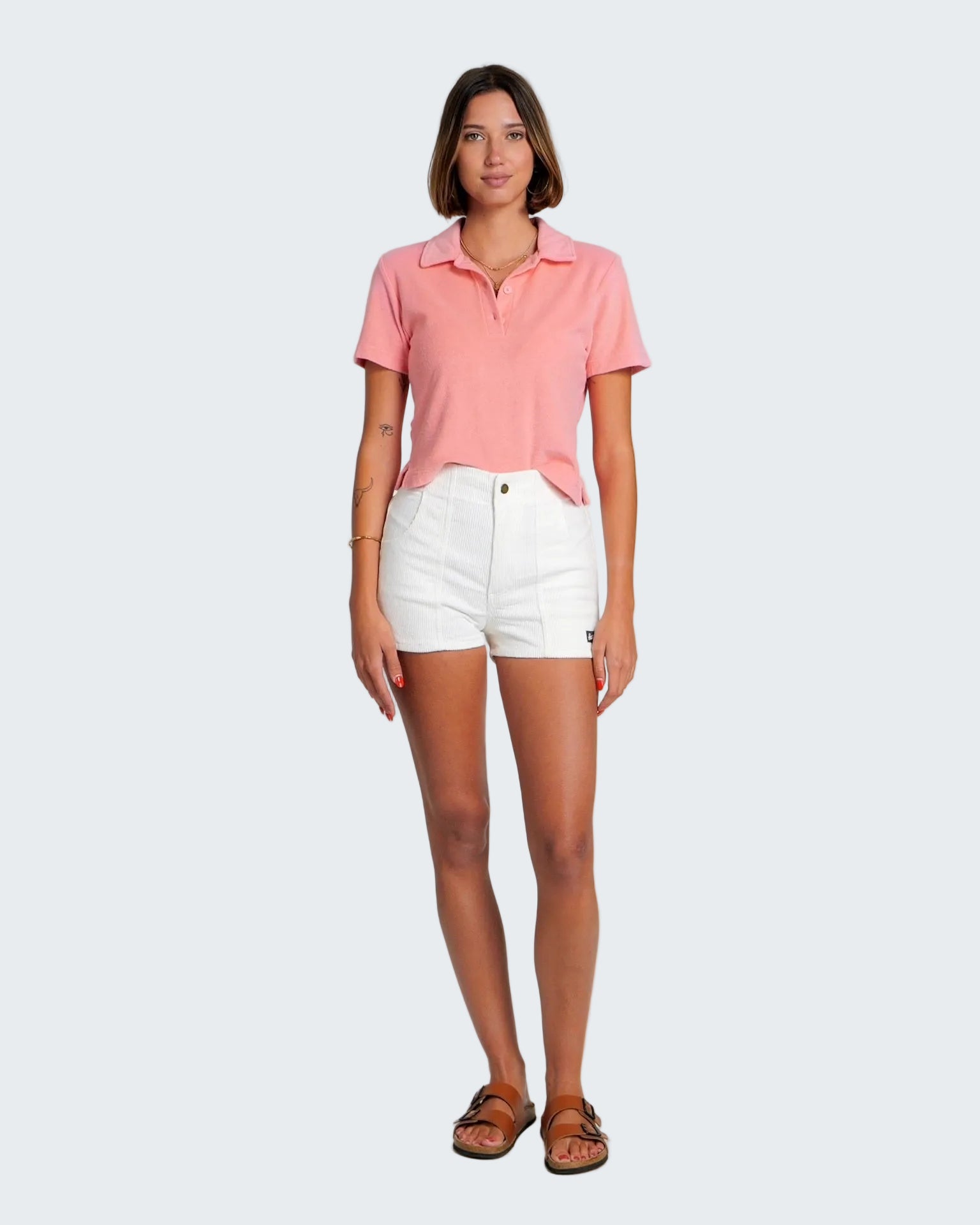 Woman wearing a pink polo shirt and white shorts on a plain background