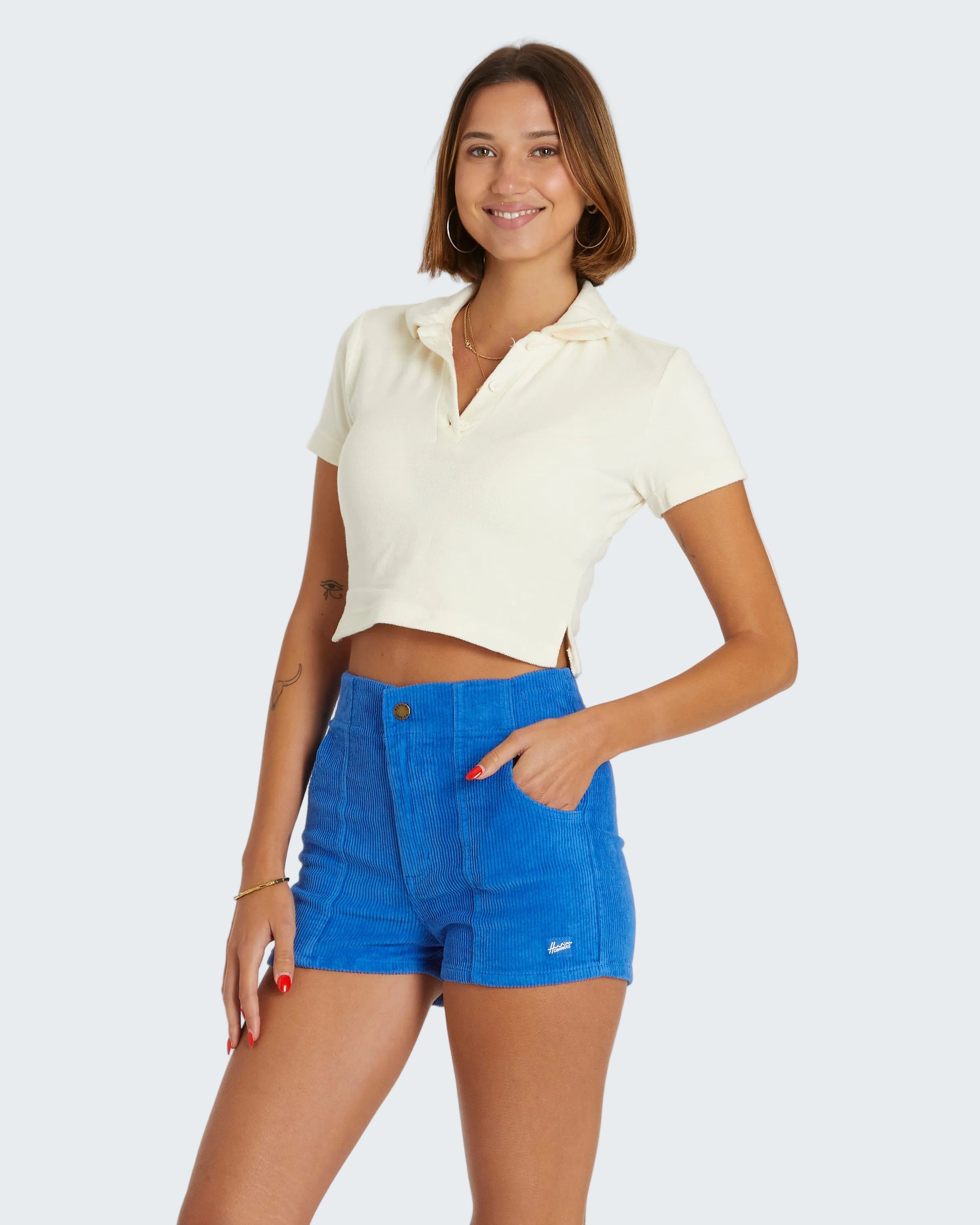 Woman wearing a white cropped top and blue shorts on a white background