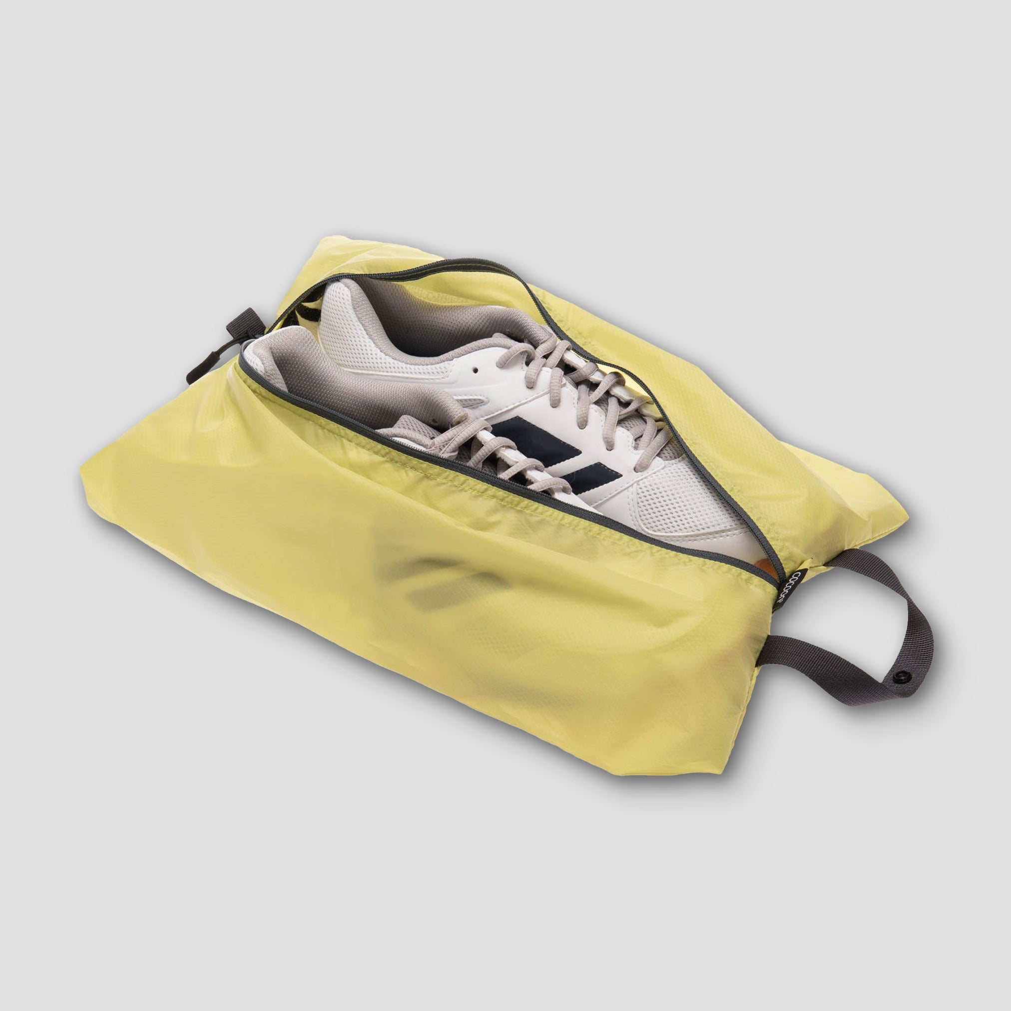 Yellow shoe bag with a white sneaker inside on a light gray background
