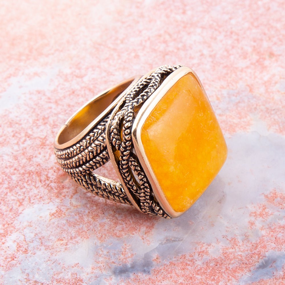 Gold and silver ring with a yellow stone on a pink marble background