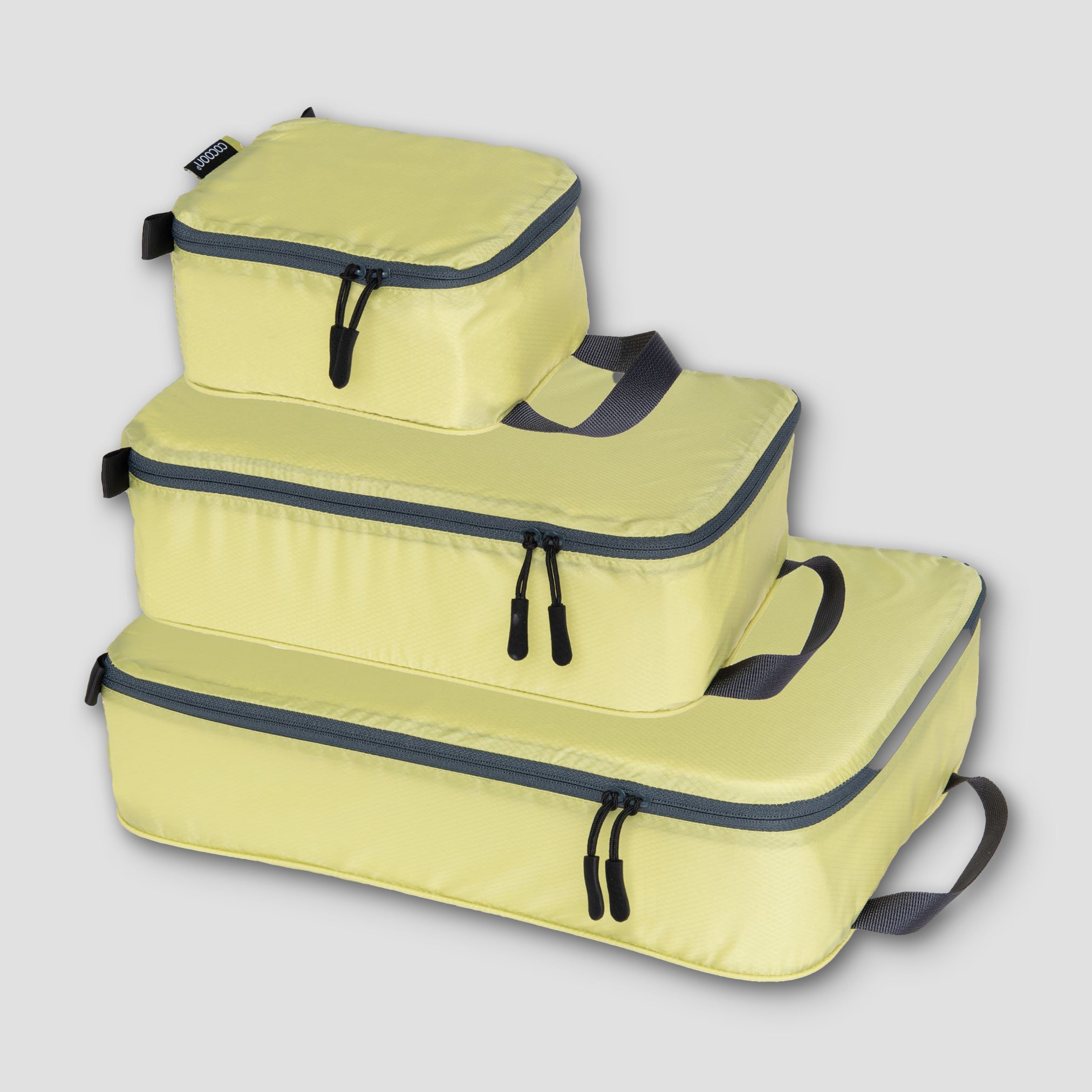 Set of three yellow packing cubes with black zippers on a light gray background