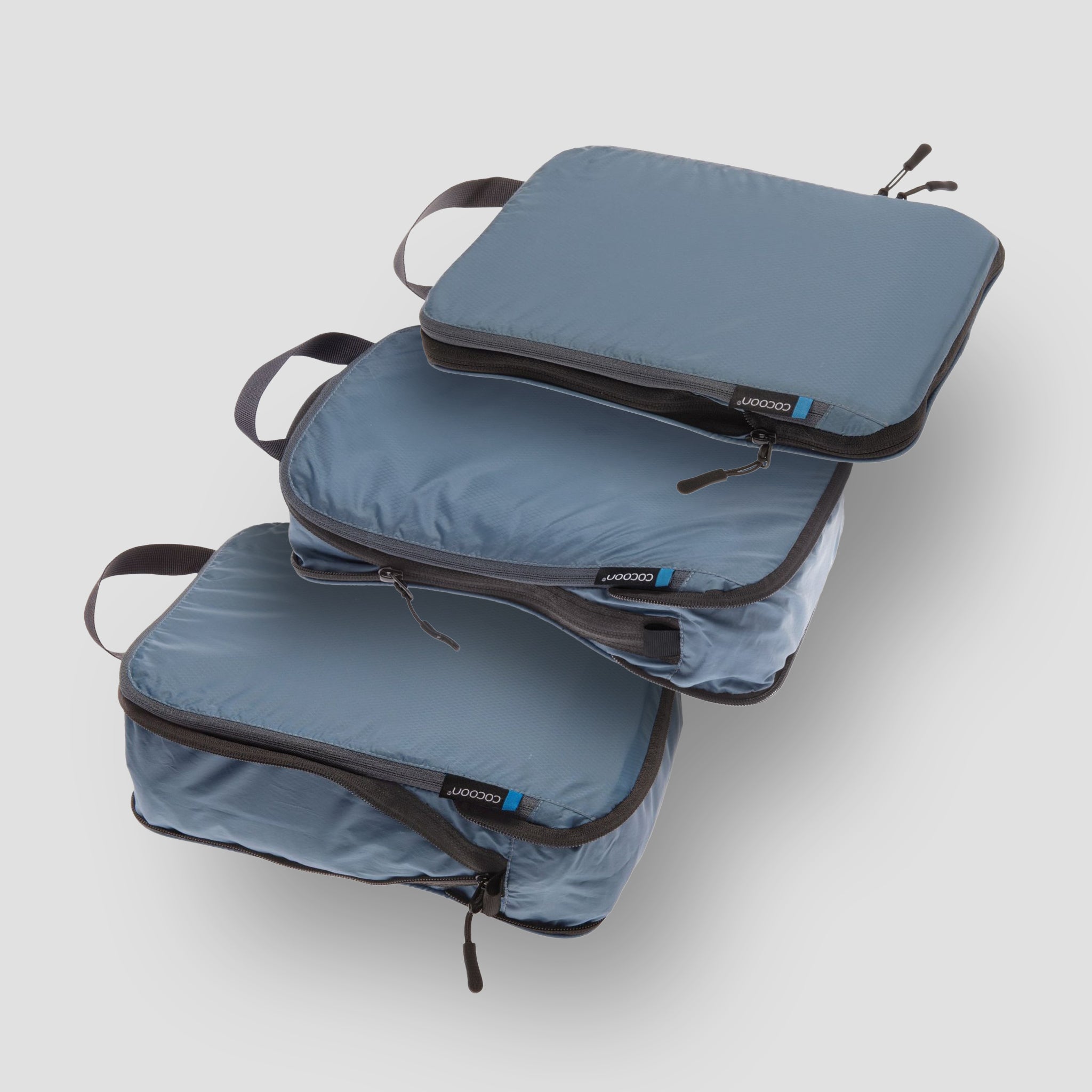 Set of three blue packing cubes with black zippers on a light gray background
