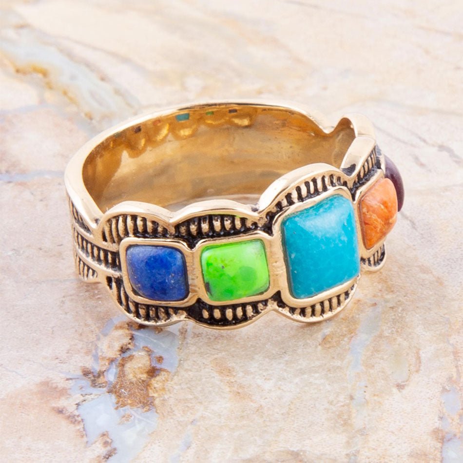 Gold ring with colorful stones on a textured beige background